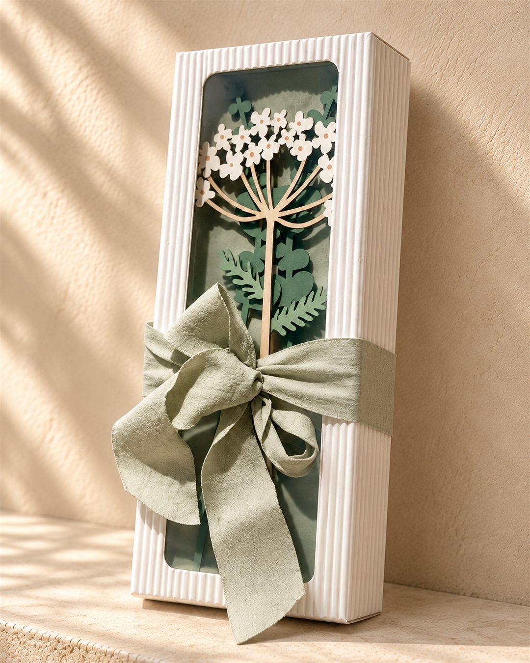 Full view of the fluted white gift box with small white wooden flowers and a sage ribbon, photographed at an angle
